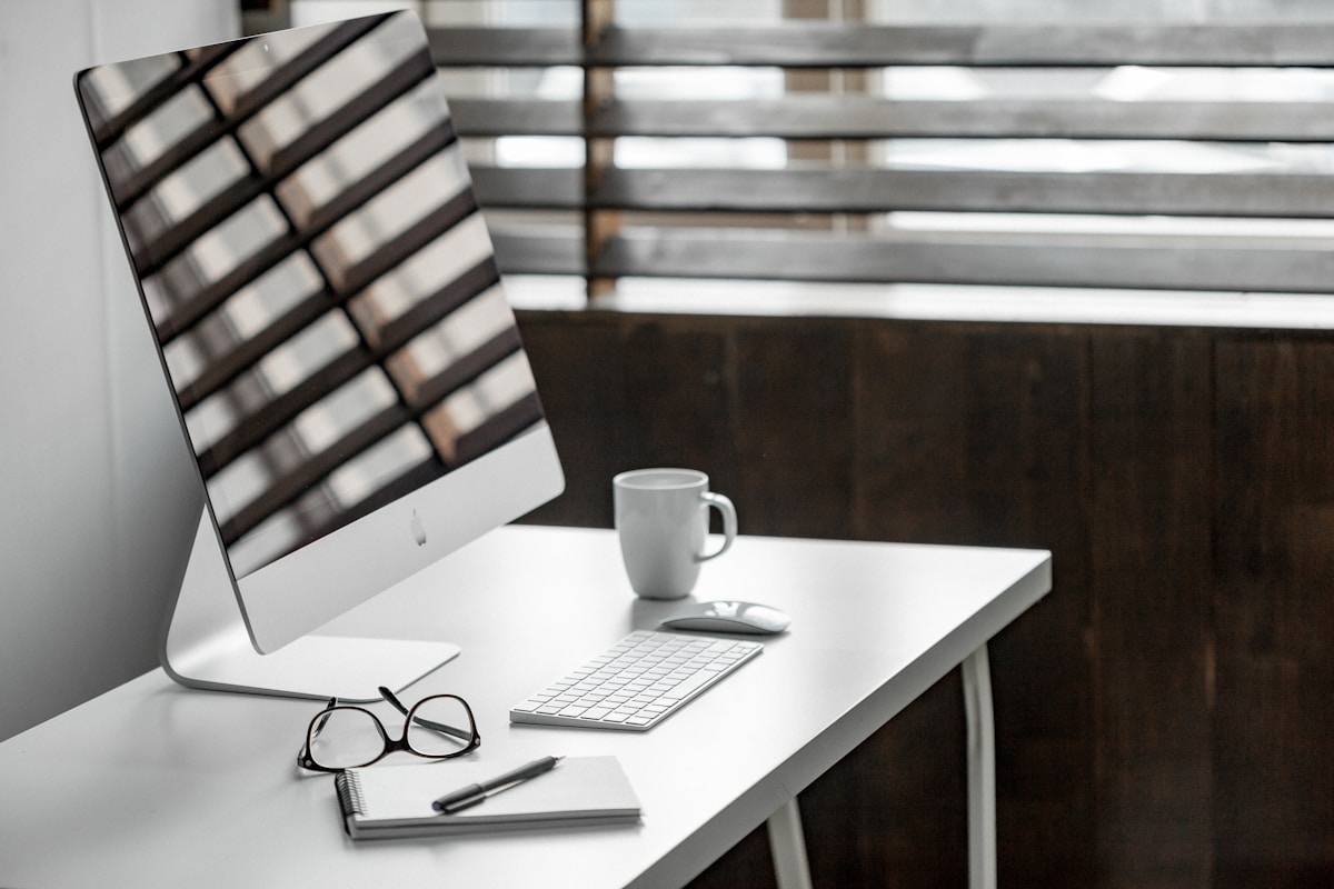 Un bureau moderne avec un ordinateur, des lunettes et une tasse de café.