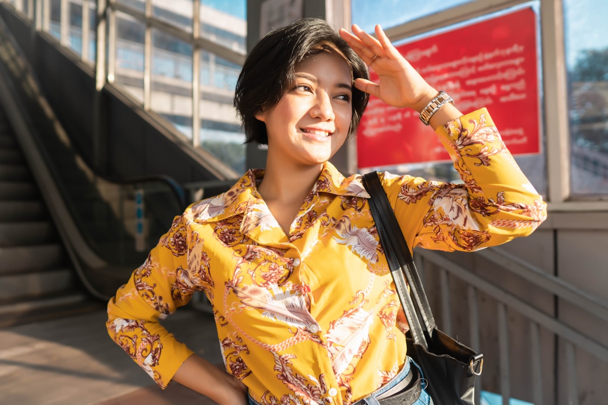 Femme souriante portant une chemise jaune à motifs floraux.