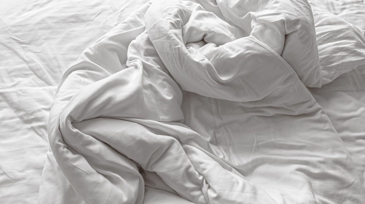 Draps blancs froissés, texture douce et accueillante.