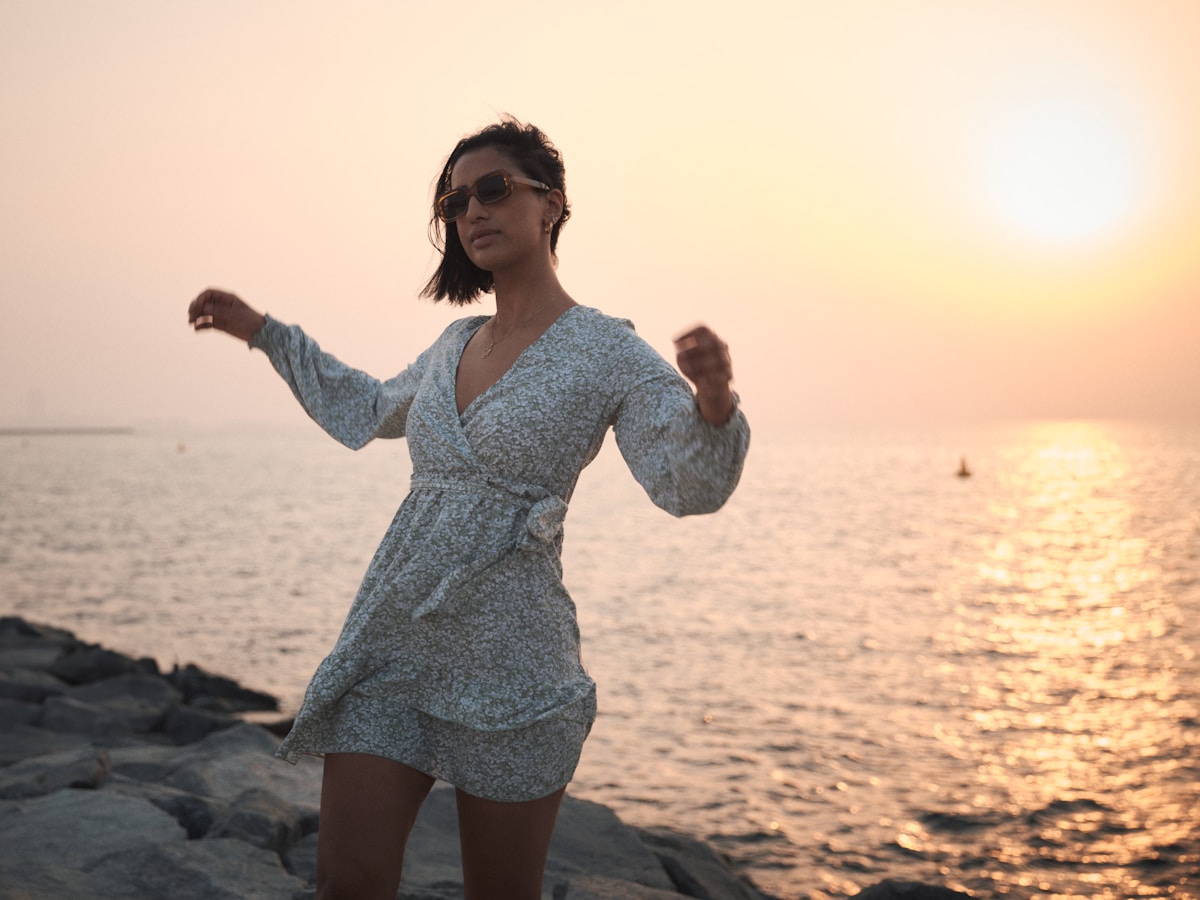Femme en robe bleue profitant du coucher de soleil sur la plage.