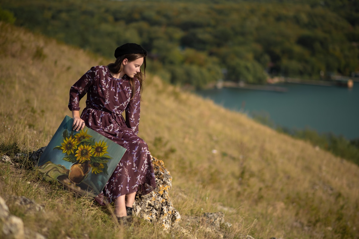 Femme en robe fleurie assise sur un rocher avec un bouquet de tournesols.