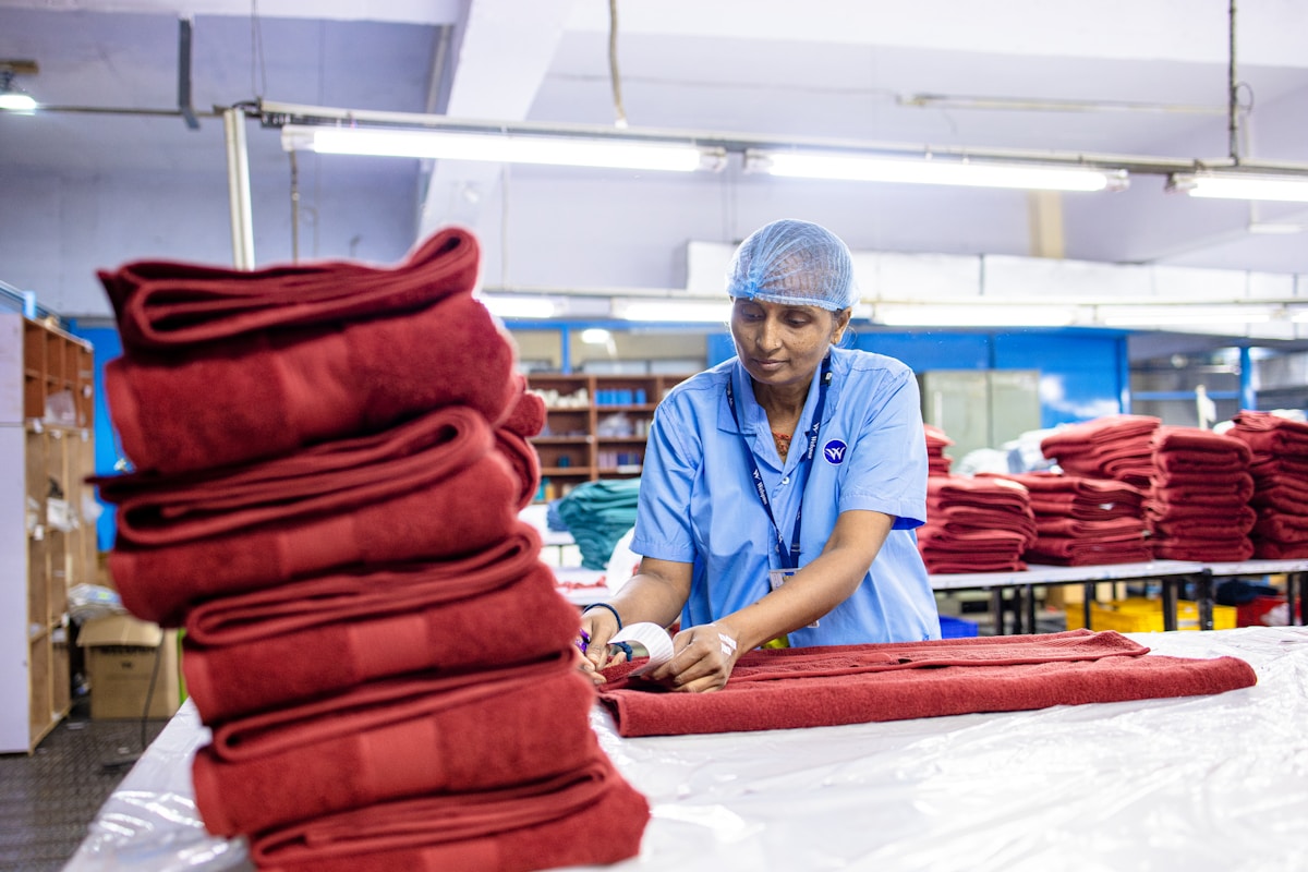 Employée dans une usine de textiles, pliage de tissus rouges.