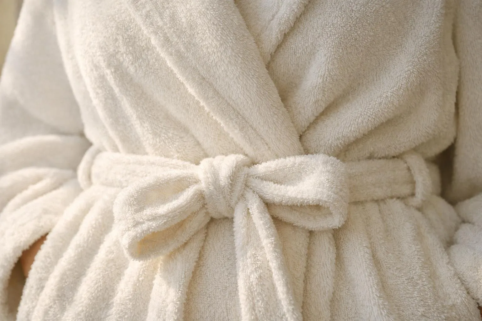Gros plan sur les détails luxueux d'un peignoir féminin: texture en coton épais, ceinture élégamment nouée à la taille, col châle raffiné, lumière douce naturelle créant une ambiance cosy et intime, palette de couleurs neutres et chaleureuses