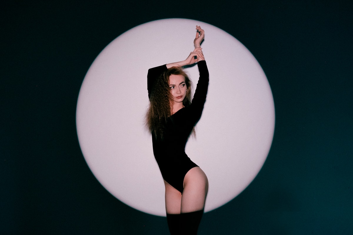 Femme en robe noire posant de manière sensuelle devant un cercle lumineux.