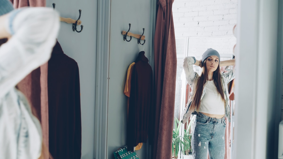 Jeune femme pensive dans un vestiaire avec des vêtements accrochés.