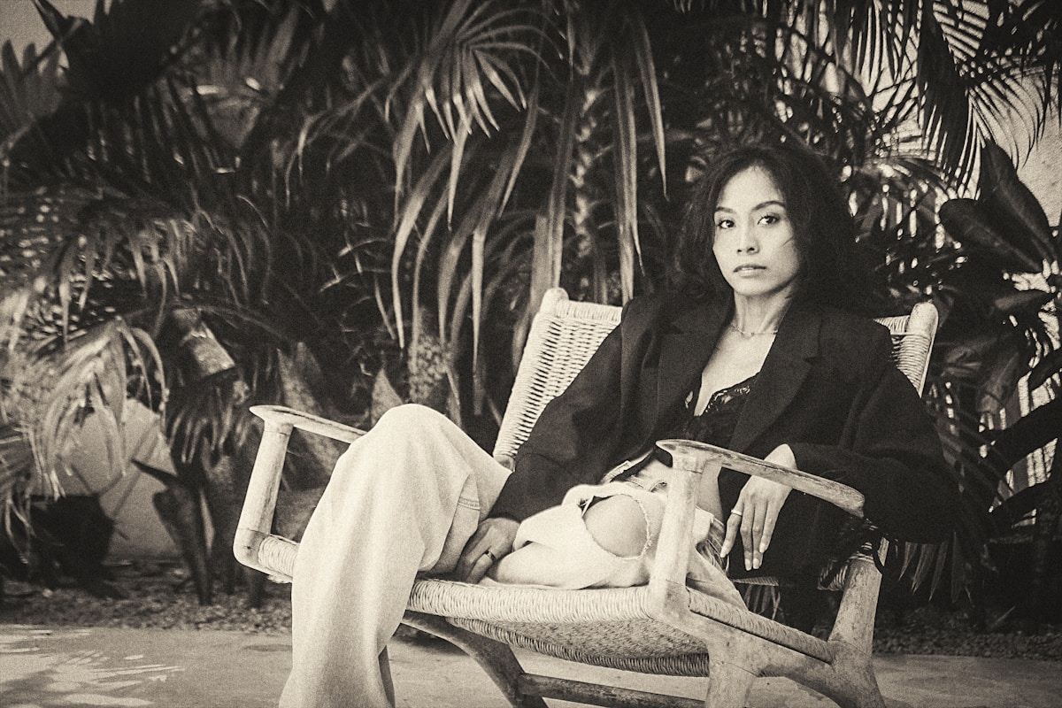 Femme assise sur une chaise en rotin dans un décor tropical.