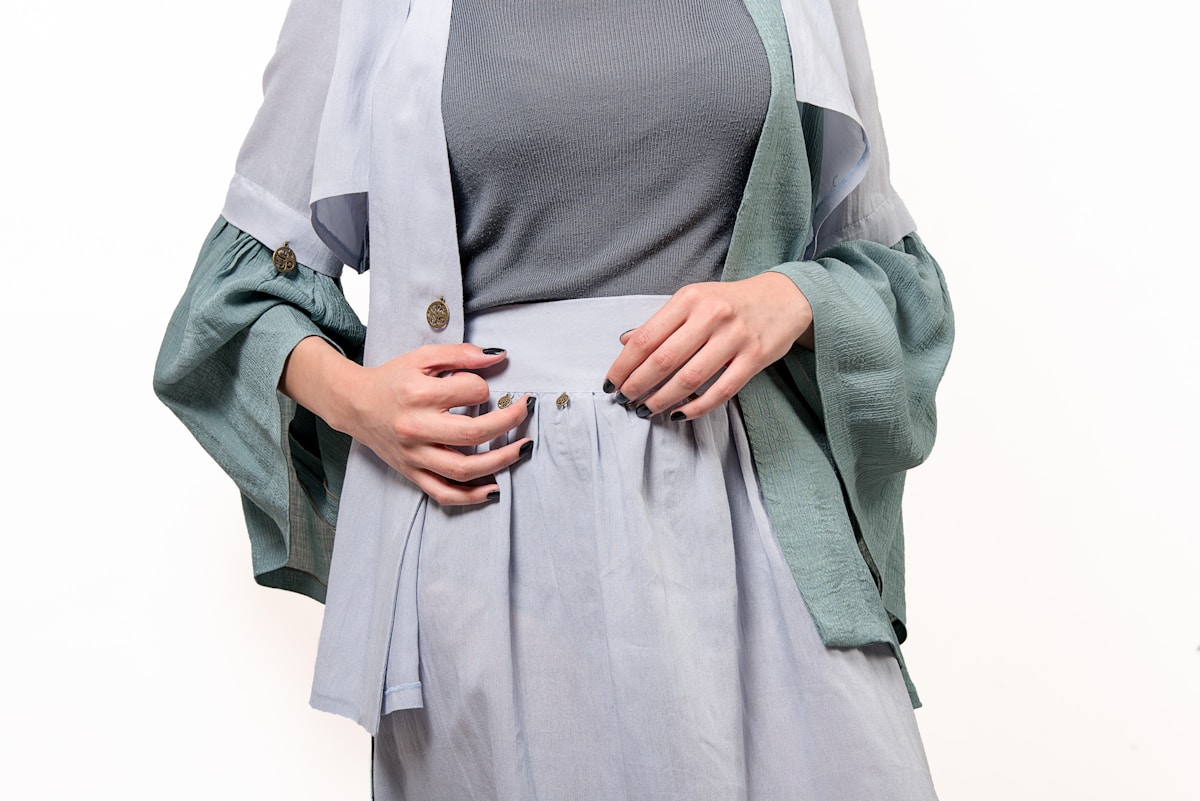 Vêtements gris et verts, manches amples, jupe plissée.