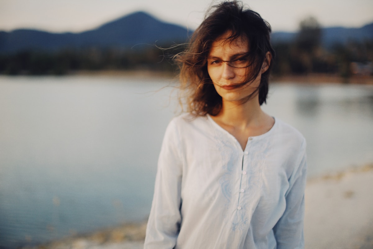Femme aux cheveux bouclés, debout devant un lac et des montagnes.