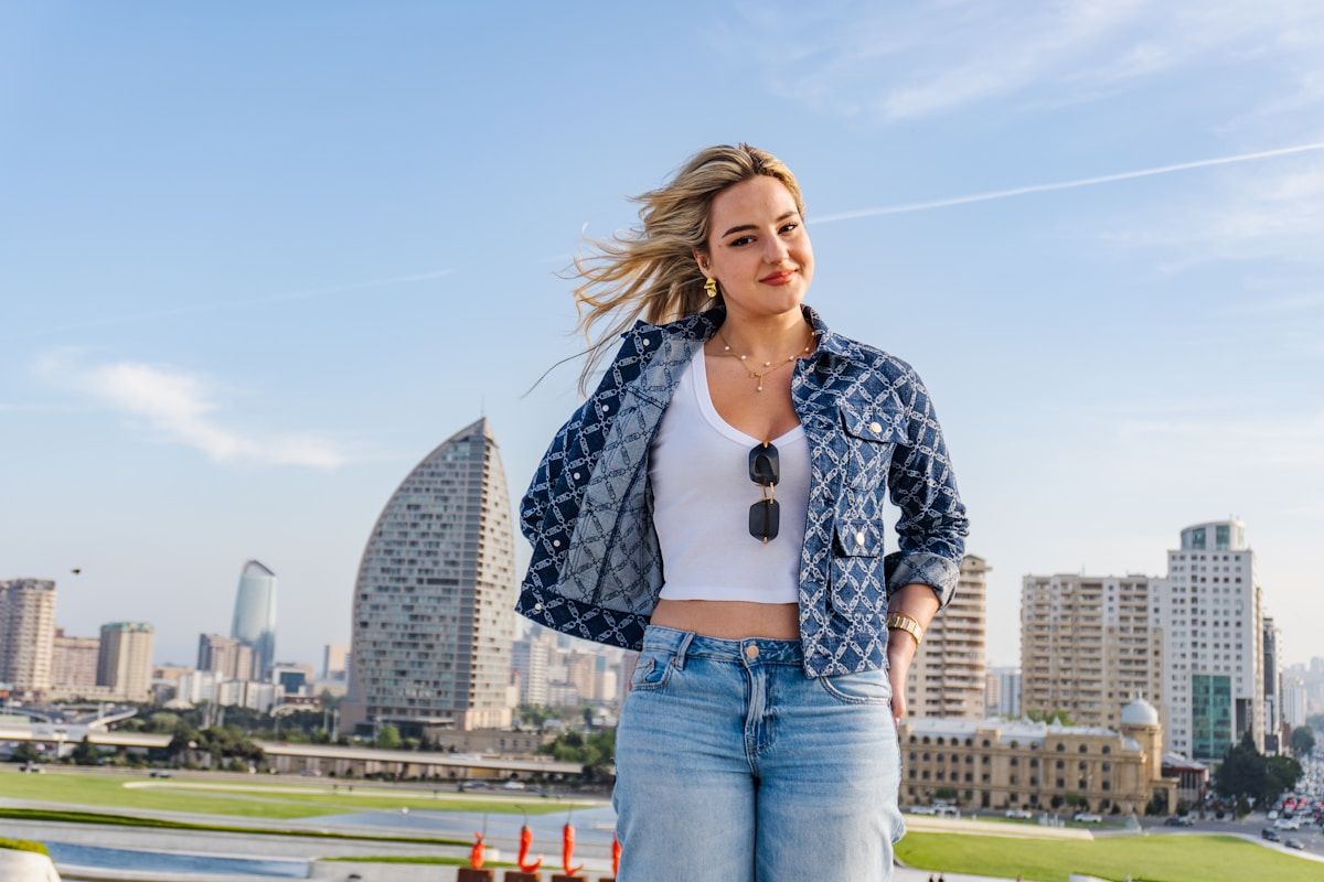 Jeune femme aux cheveux blonds dans une veste en jean devant un paysage urbain.