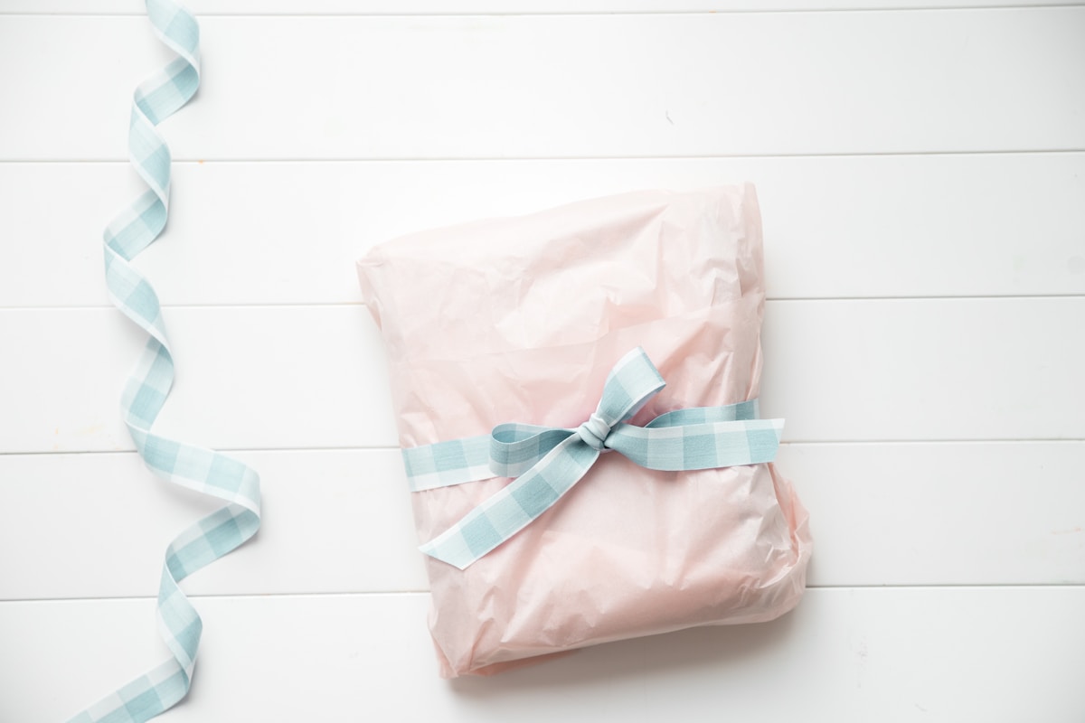 Paquet cadeau rose avec ruban bleu sur fond blanc.