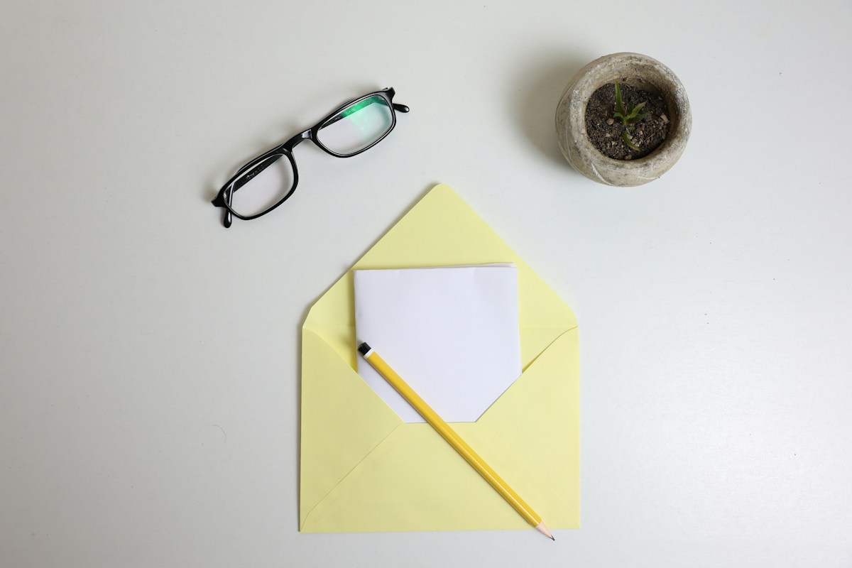 Enveloppe jaune, crayon, lunettes et plante sur bureau blanc