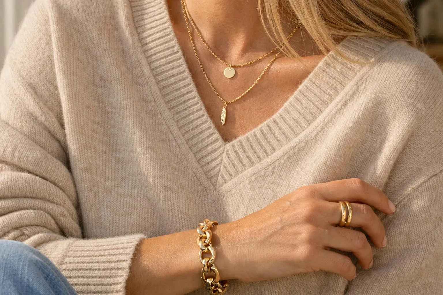 Femme portant un pull beige, colliers et bracelets dorés.