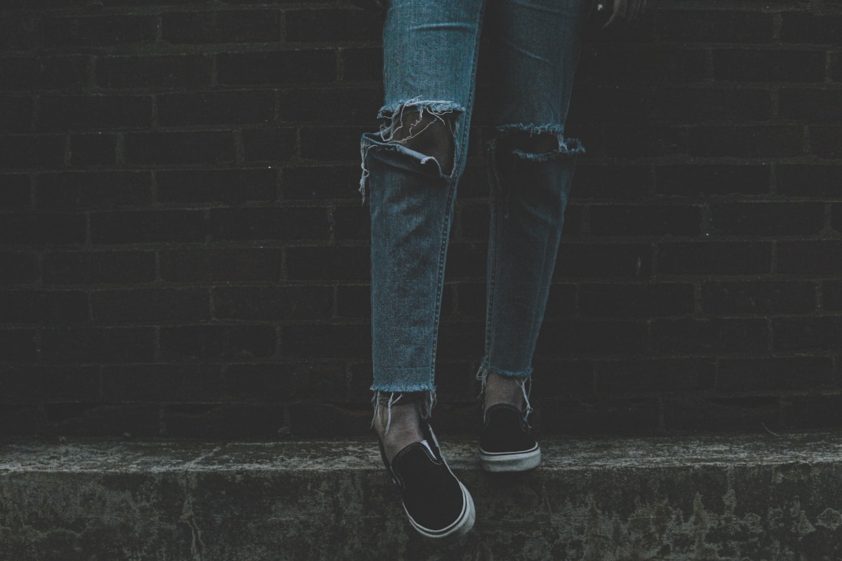 person wearing distressed blue denim jeans and pair of black-and-white sneakers