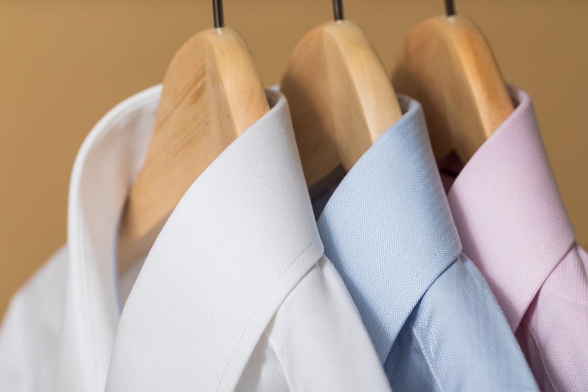 Chemises blanches, bleues et roses suspendues sur des cintres.