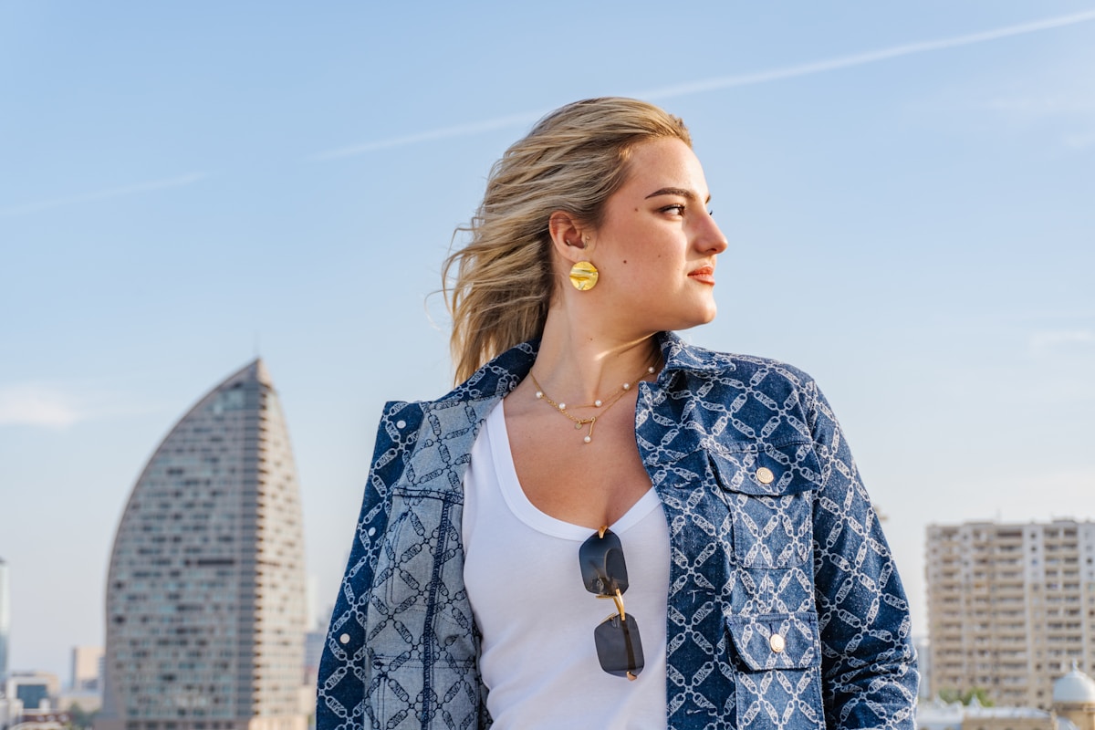 Femme blonde portant un manteau à motifs bleus avec des boucles d'oreilles jaunes.