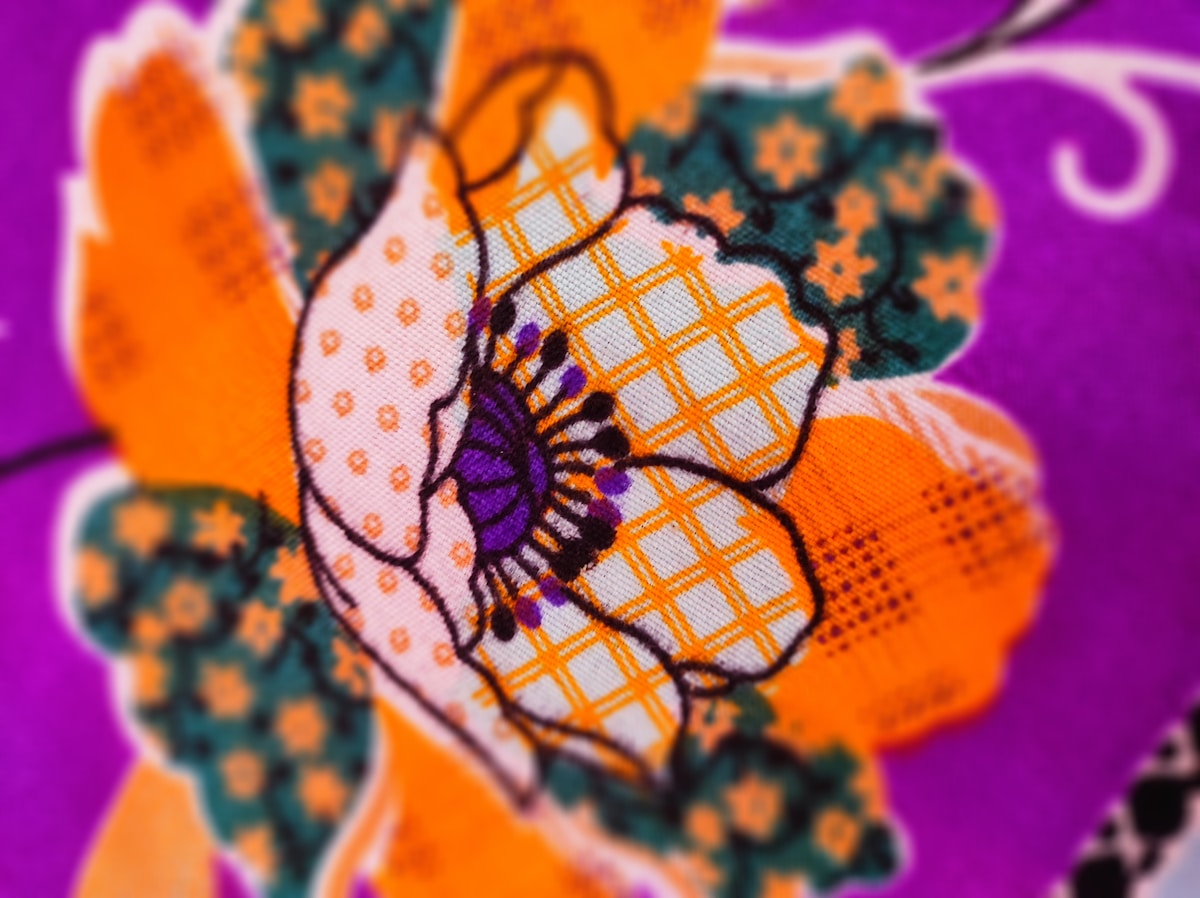 Fleur brodée aux motifs colorés et géométriques sur fond violet.
