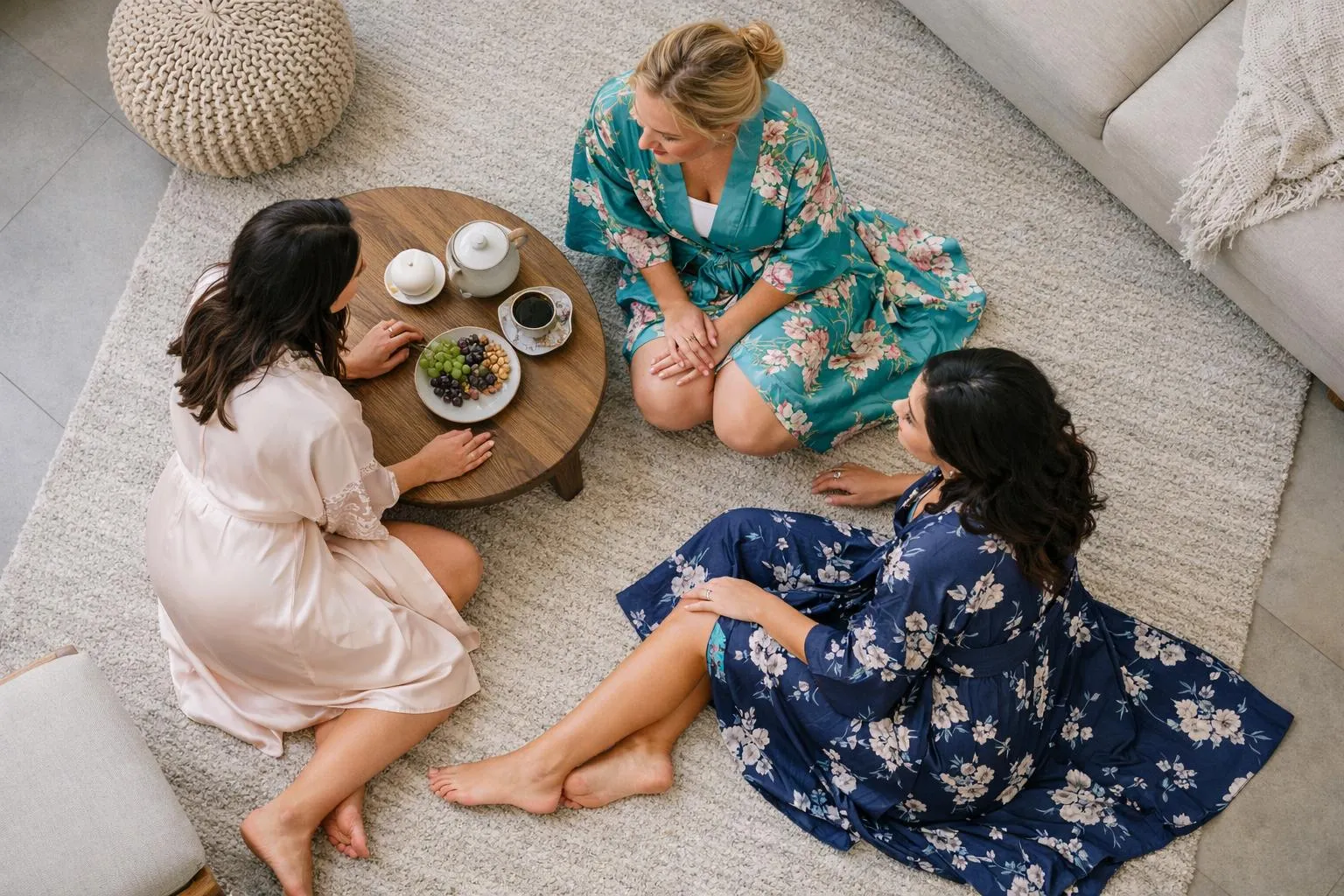 Trois femmes en peignoirs fleuris, assises sur un tapis moelleux, partageant un moment de détente.
