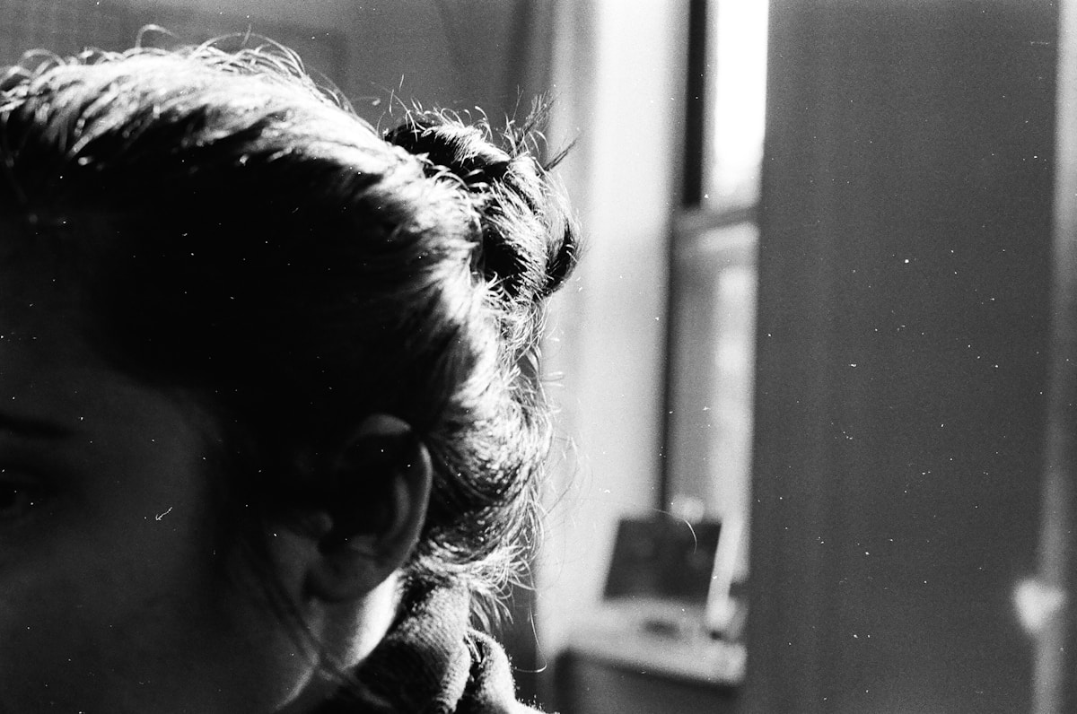 a black and white photo of a woman looking out a window