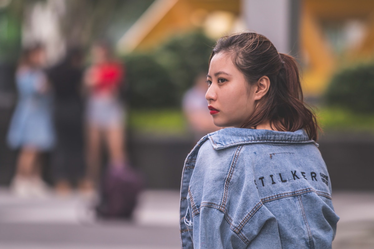 Jeune femme asiatique portant une veste en jean avec le mot "Tilker" écrit dessus.