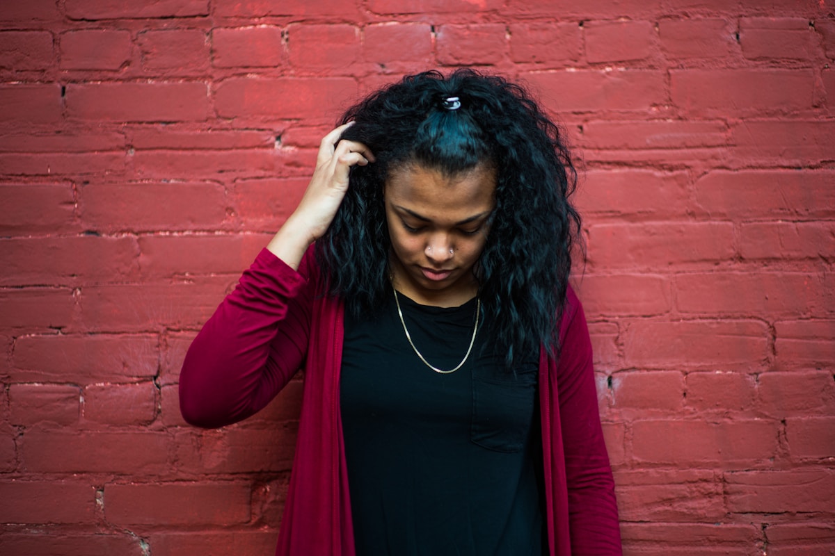 Jeune femme aux cheveux bouclés, portant un manteau rouge, debout devant un mur de briques.