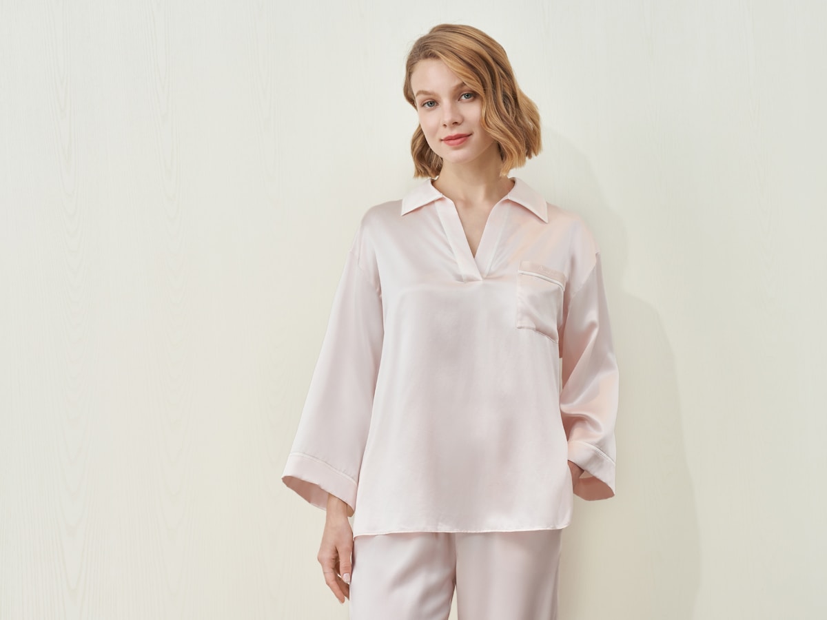 Femme blonde aux cheveux courts portant une chemise rose clair.