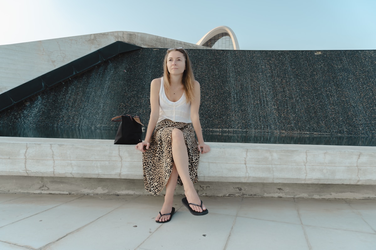 Femme debout devant un bâtiment moderne, vêtue d'un haut blanc et d'une jupe léopard.