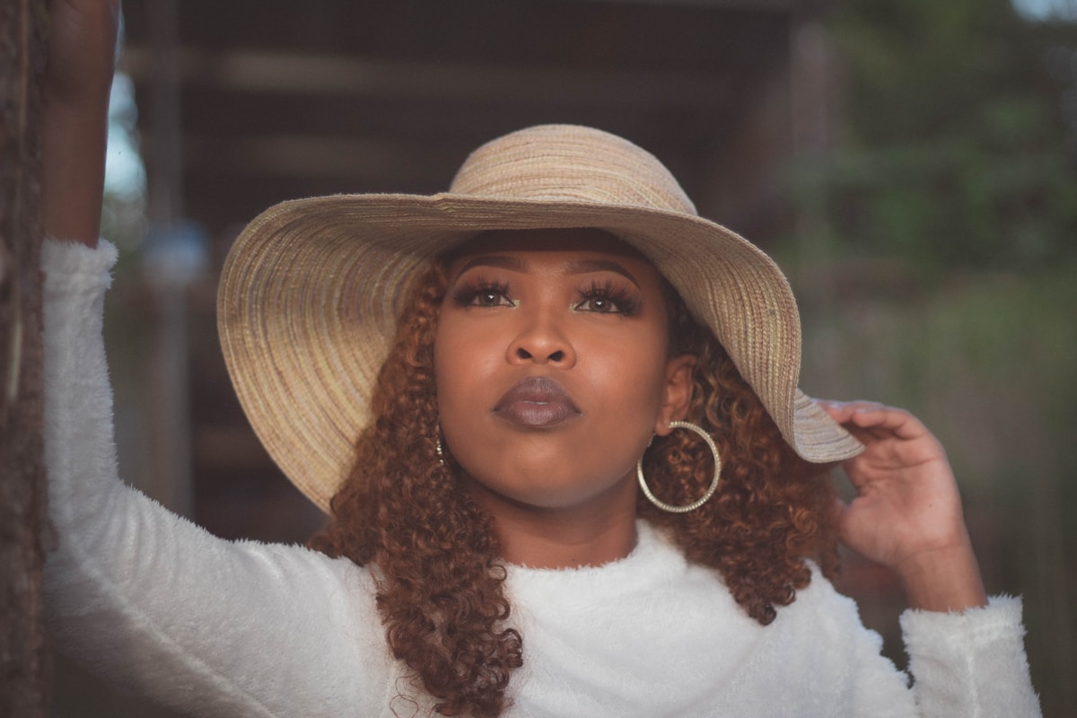 Femme aux cheveux bouclés portant un chapeau de paille et des boucles d'oreilles.