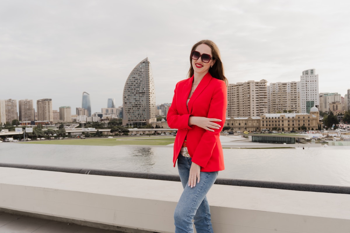 Femme en manteau rouge posant devant un paysage urbain.