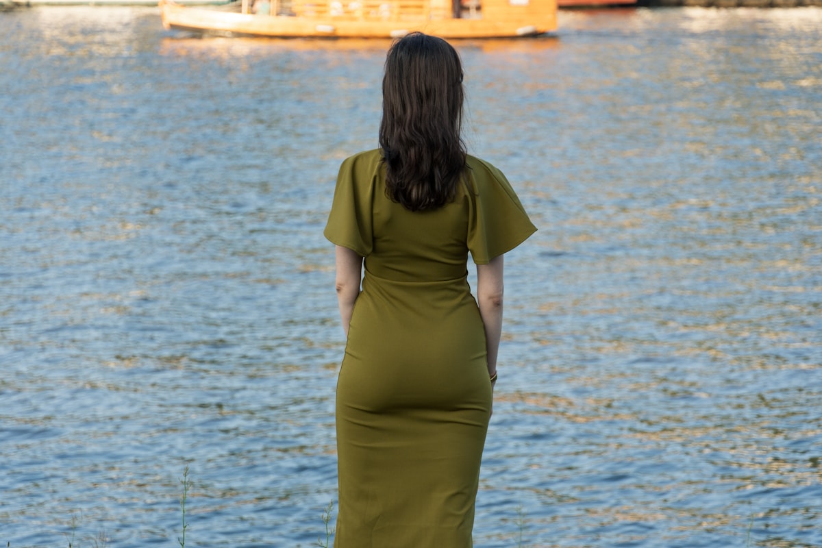 Femme en robe verte debout près de l'eau.