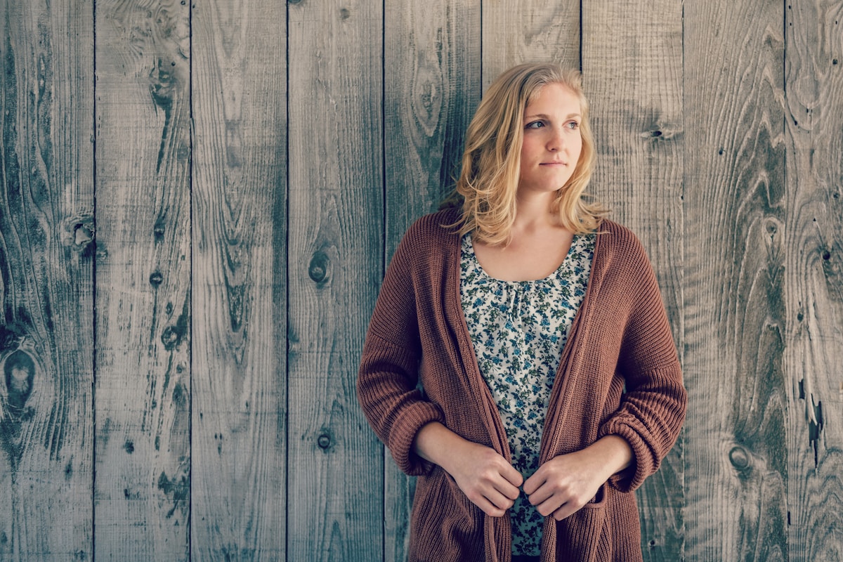 Jeune femme blonde portant un cardigan brun devant un mur de bois.