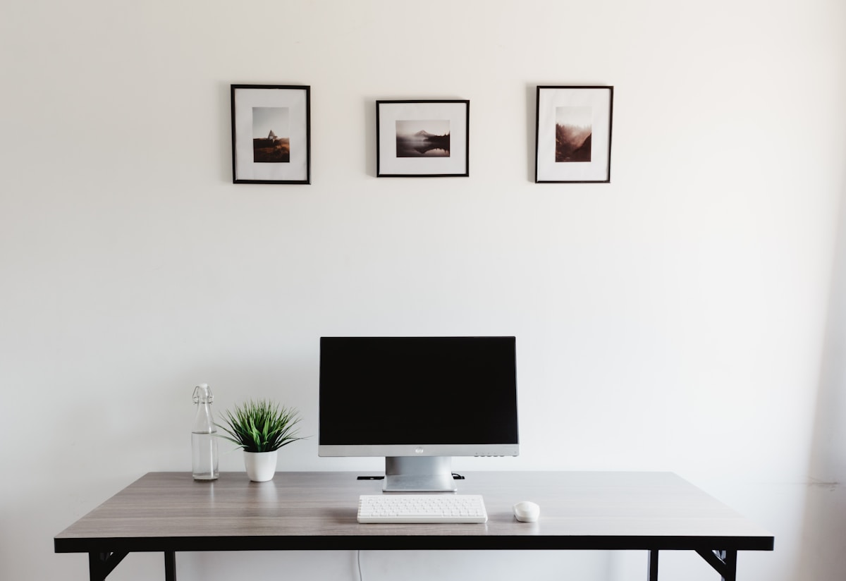 Bureau minimaliste avec écran d'ordinateur, plante verte et cadres muraux.