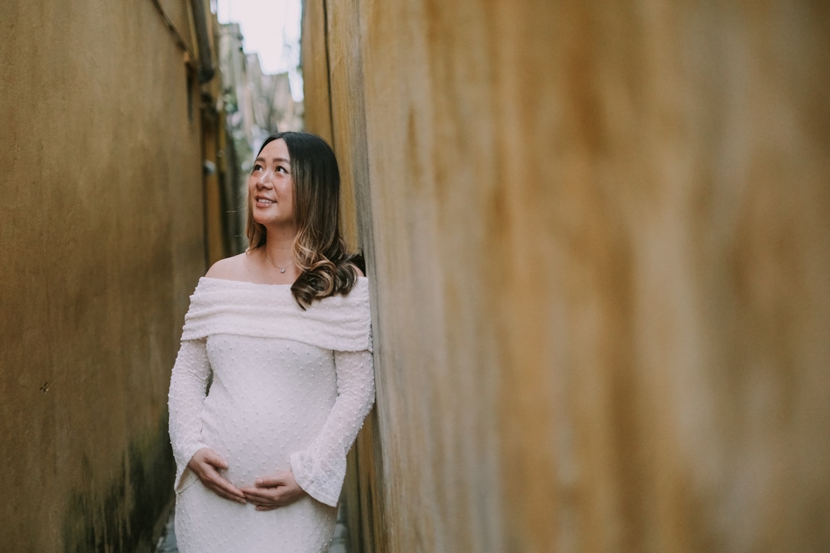 Pregnant woman in white dress in narrow alley.