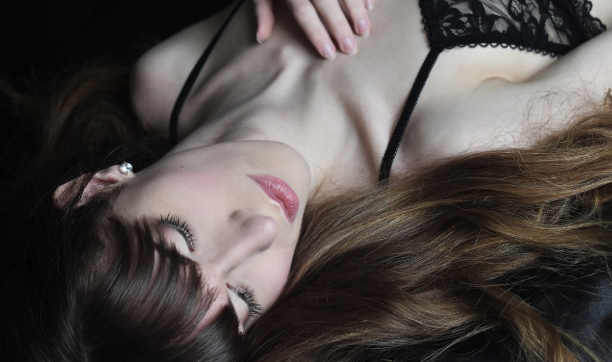 Femme allongée, vêtements noirs, cheveux longs, maquillage, expression pensive.