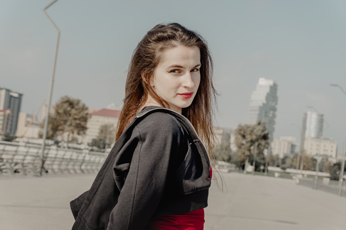 Jeune femme aux cheveux bruns, vêtue d'un manteau gris, debout dans une ville.