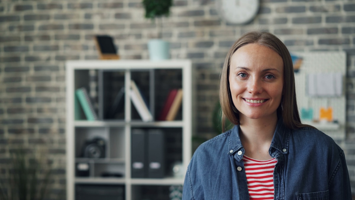 Femme souriante dans un bureau moderne avec étagère.