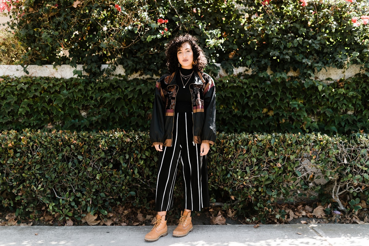 Femme aux cheveux bouclés portant un manteau fleuri et des bottes.