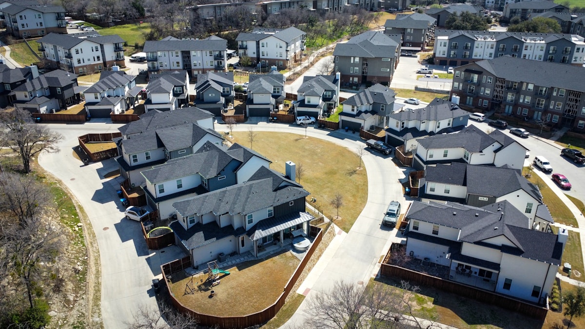 Quartier résidentiel avec maisons et appartements, voitures garées, arbres et espaces verts.