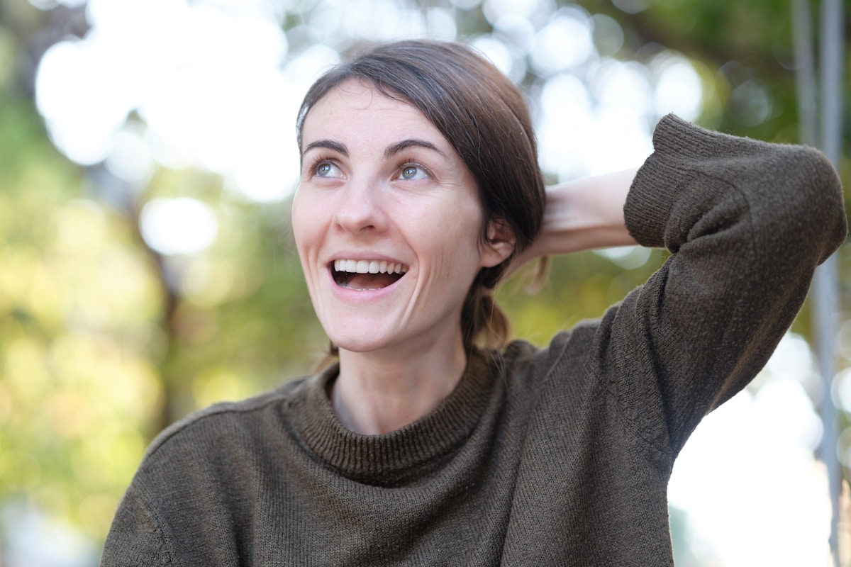 Femme souriante, heureuse, en pull vert, dans un cadre naturel.