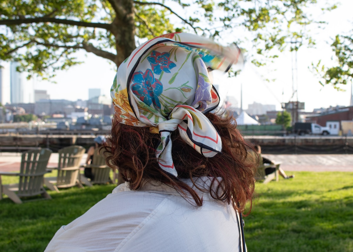 Femme aux cheveux bouclés portant un foulard fleuri dans un parc verdoyant.