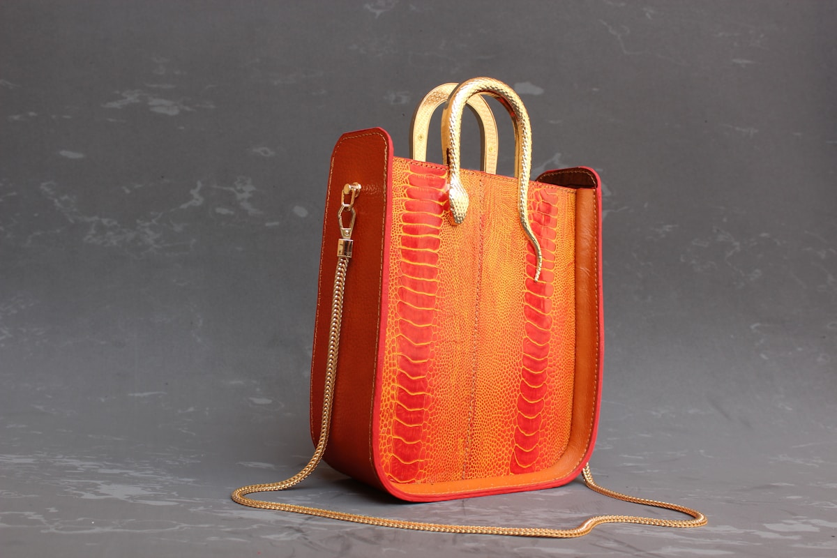 Sac à main en cuir orange vif avec motif reptilien et chaîne dorée.