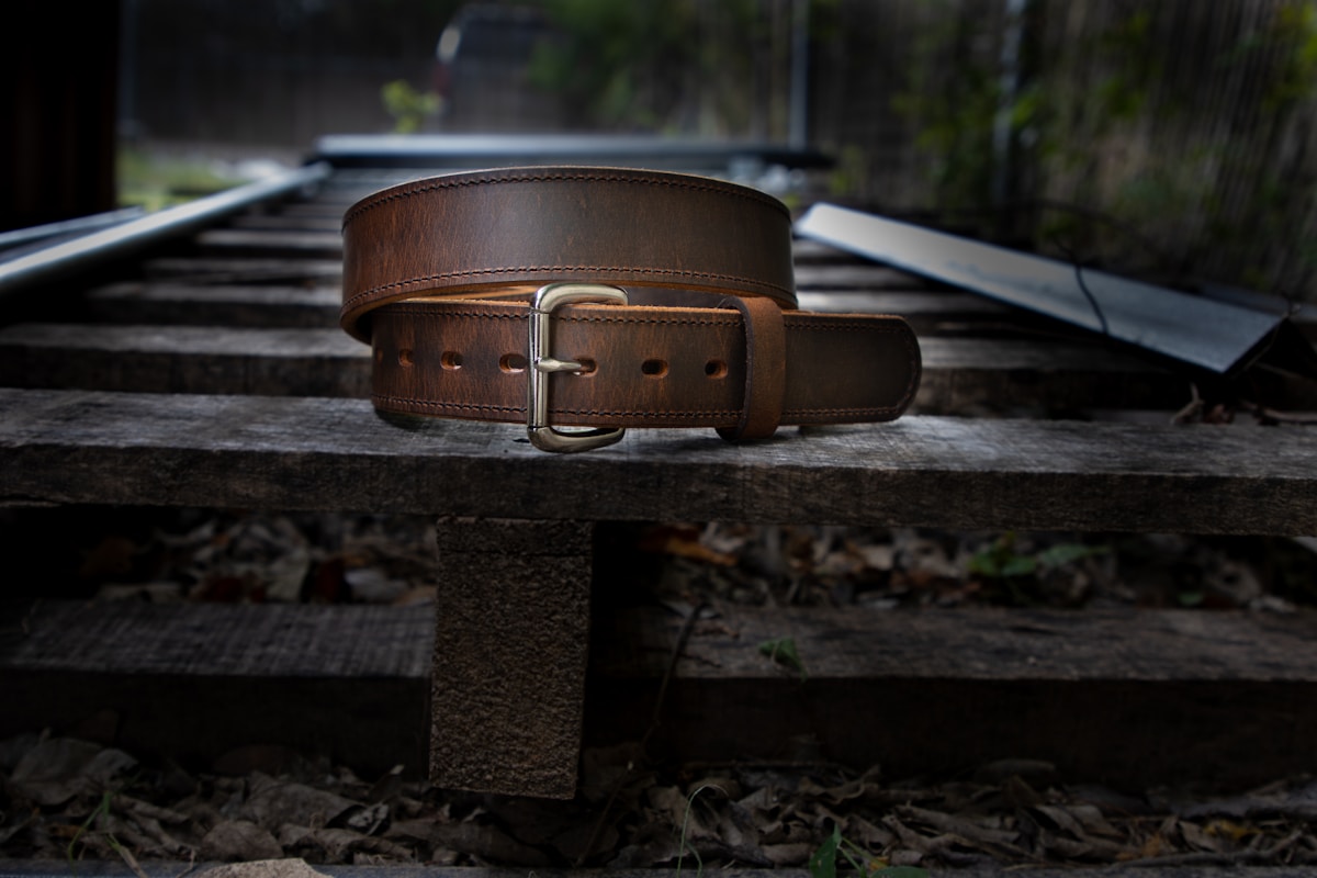 Ceinture en cuir marron avec boucle métallique sur un banc en bois.