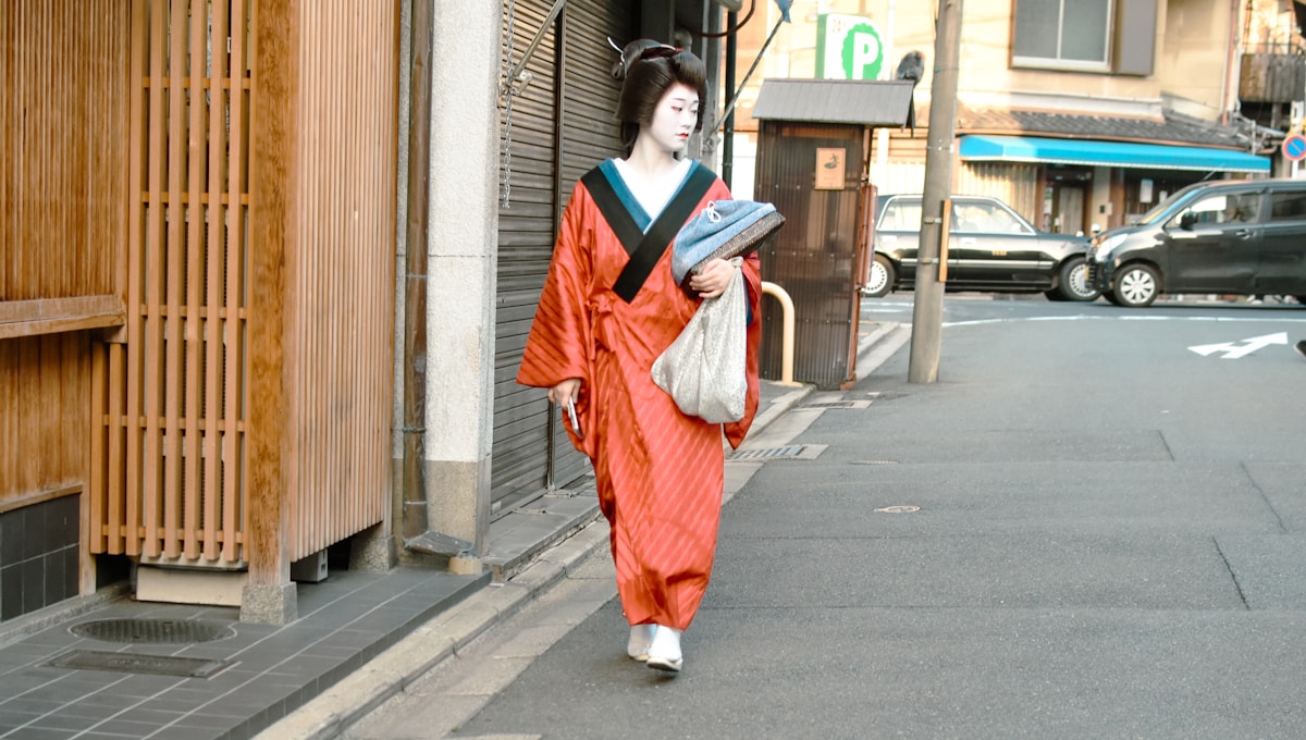 A geisha walks down a street in traditional dress.