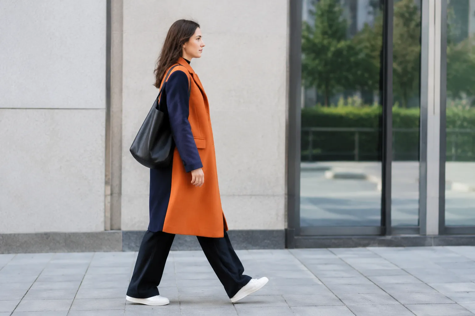 Femme marchant en manteau orange, pantalon noir et sac cabas.