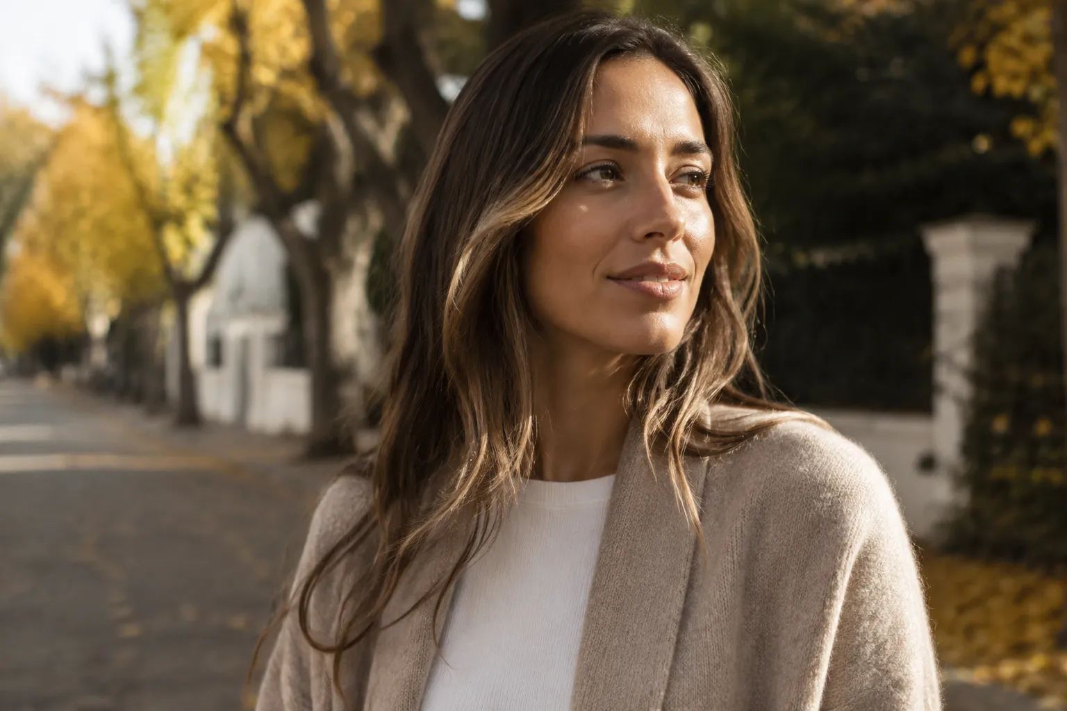 Femme aux cheveux longs et bruns, vêtue d'un pull beige, dans un cadre automnal.