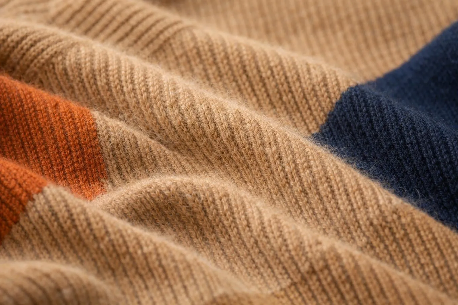 Close-up macro view of luxurious merino wool sweater fibers in warm caramel tones, showing the delicate texture and natural crimp of fine wool, soft focus with cozy winter lighting highlighting the fiber structure and plush quality