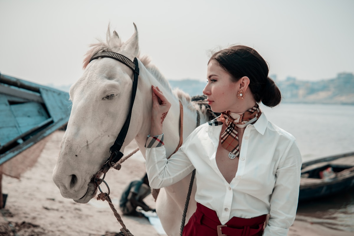 Femme élégante caressant un cheval blanc près de l'eau.