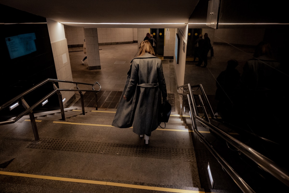 Femme en manteau marchant dans un couloir sombre et désert.