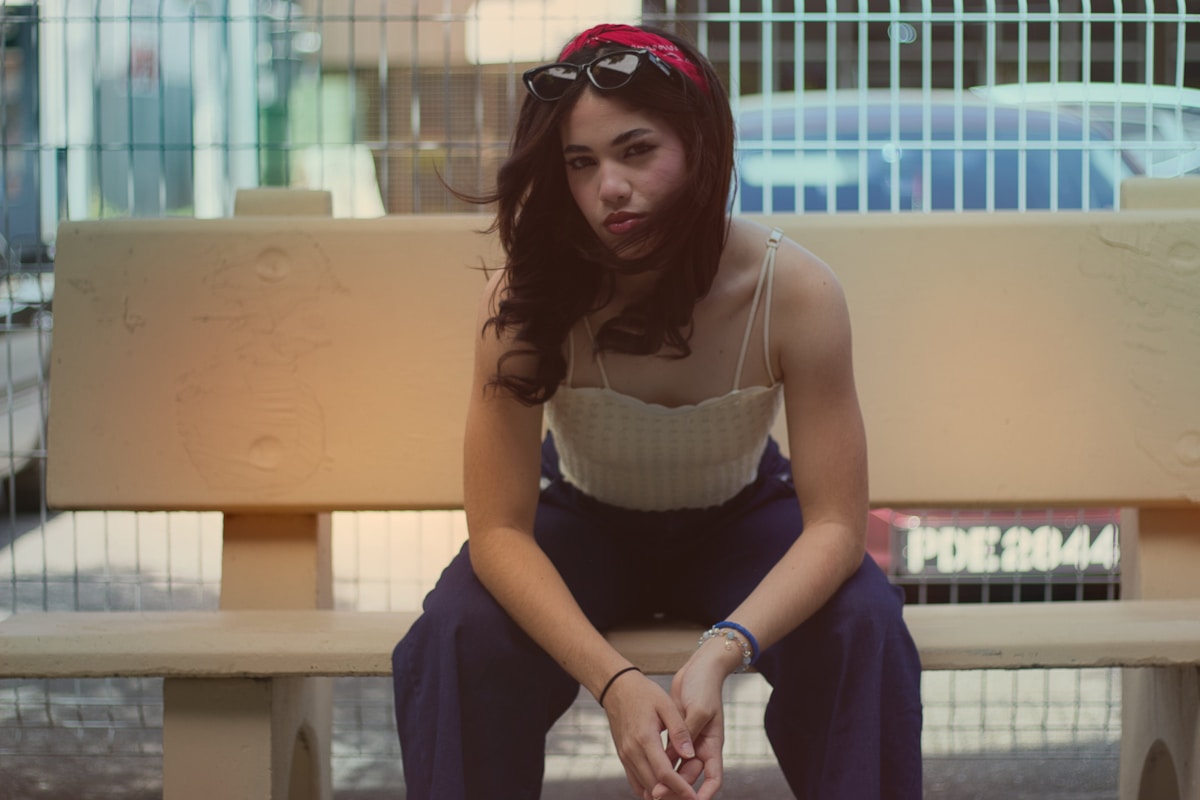 Jeune femme assise, vêtements colorés, expression pensive.