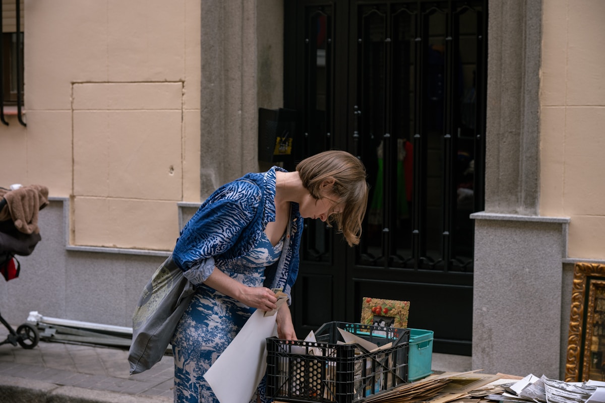 Femme en robe bleue portant des boîtes et des objets dans un couloir.