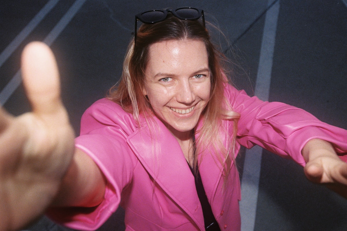 Femme souriante en veste rose vif, cheveux au vent.